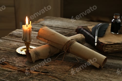 Preview: Old paper scrolls, book, feather, inkwell and burning candle on wooden table, closeup