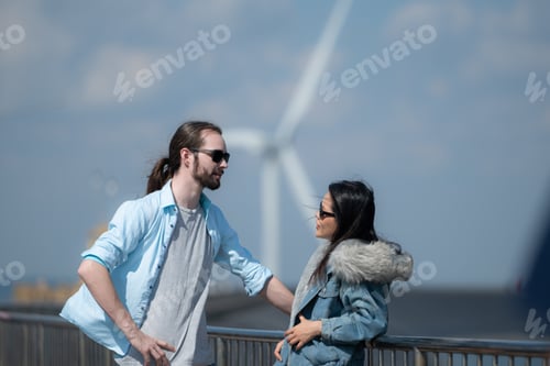 Preview: Young couple relaxing by the wind turbine on the lake