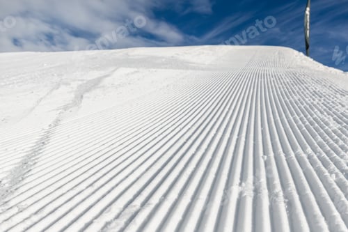 Preview: Close-up straight line rows of freshly prepared groomed ski slope piste with bright shining sun and
