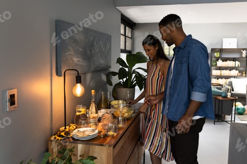 Preview: Couple preparing snacks and drinks at home for evening celebration