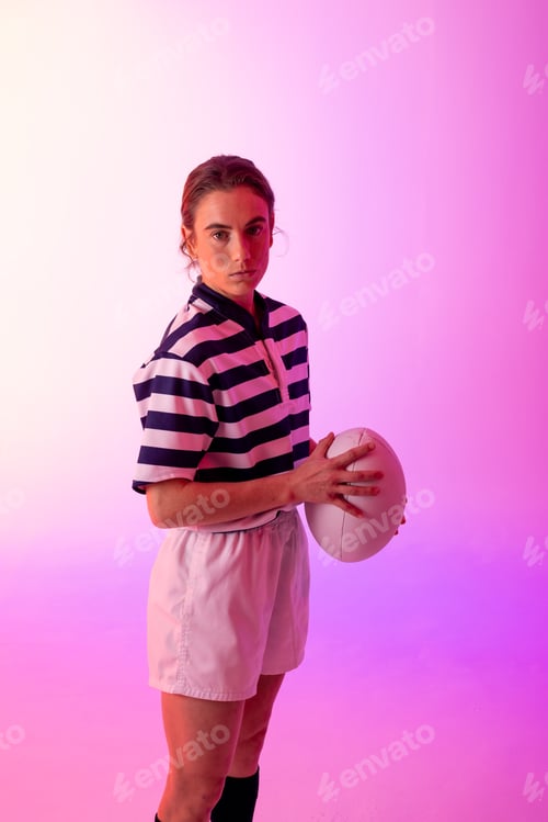 Preview: Portrait of caucasian female rugby player with rugby ball over neon pink lighting