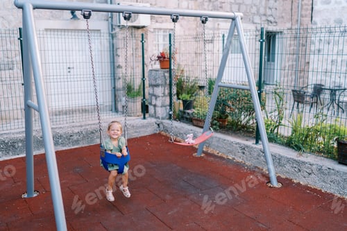 Preview: Little girl sits on a gray chain swing in the yard of a house