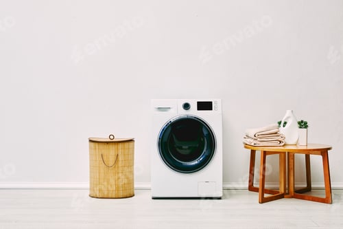 Preview: white washing machine near laundry basket, coffee table with towels, detergent bottle and plant in