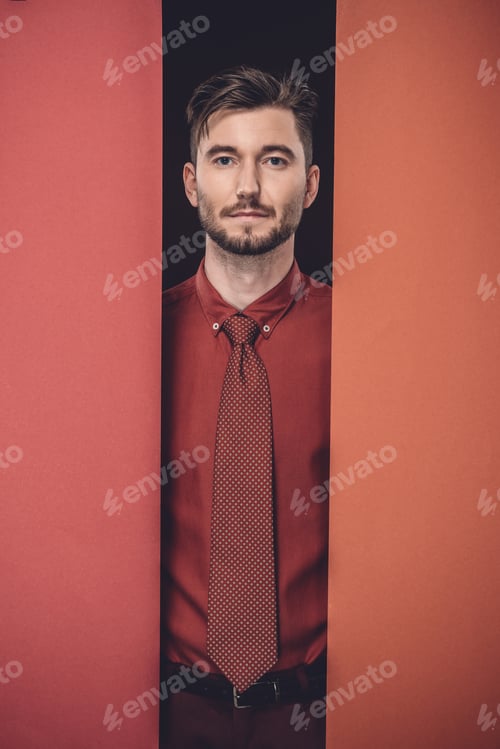 Preview: Young businessman in red shirt by red paper walls isolated on black