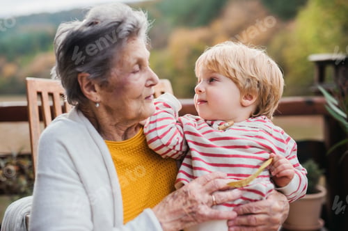 Preview: Elderly woman with a toddler great-grandchild on a terrace in autumn.