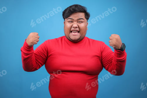 Preview: Portrait Of Attractive Fat Man Gesture Celebration Raising Fist Isolated On Blue Background