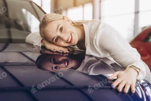 Preview: Positive young caucasian woman hugging his new car in dealership