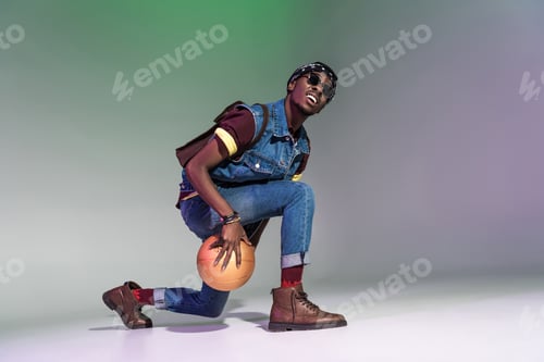 Preview: stylish young african american man playing with golden basketball ball on grey