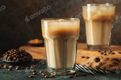 Preview: Ice coffee in a tall glass with cream poured over, ice cubes and beans on a dark concrete table.