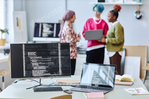 Preview: Close up of two computer screen with code lines and blurred creative team