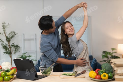 Preview: Young asian couple enjoying a lively dance while preparing fresh organic vegetables and fruits for a