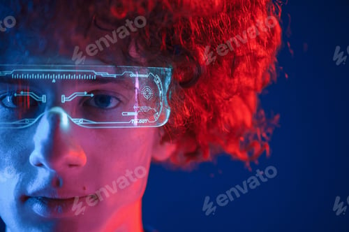 Preview: In futuristic eyewear. Young man with curly hair is indoors illuminated by neon lighting