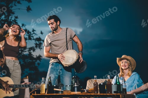 Preview: Group of young male and female friends enjoying under night sky near lake while partying