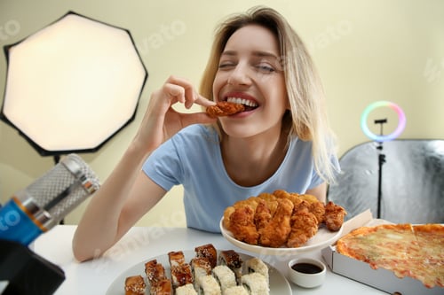 Preview: Food blogger eating in front of microphone at table against light background. Mukbang vlog