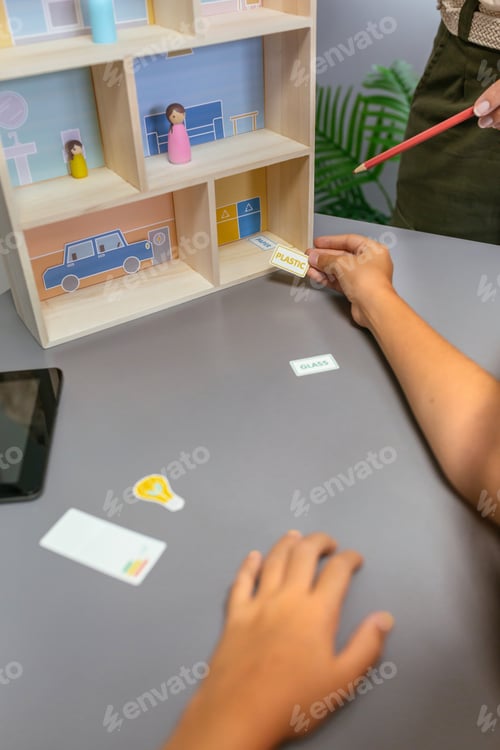 Preview: Unrecognizable teacher teaching recycling with toy house to a female student in an ecology classroom