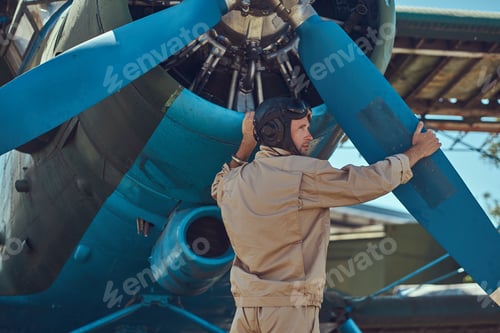 Preview: Pilot or mechanic in a full flight gear next to retro military aircraft