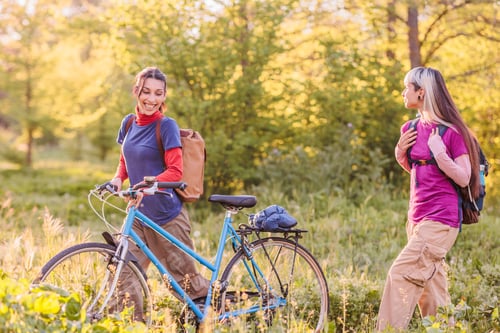 Preview: Two female friends hiking and cycling in nature during golden hour