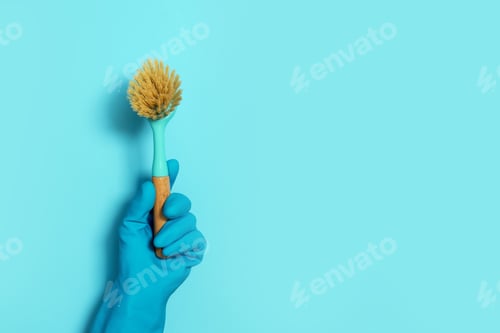 Preview: Hand in glove holding brush on blue background. Copy space. Cleaning house, cleaning toilet concept