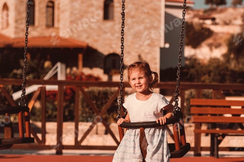 Preview: Cute toddler girl having fun on playground, swinging in sunny summer day. Smiling happy little girl