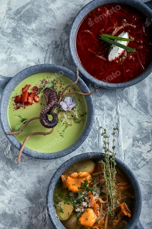 Preview: Gray plates with different soups on a gray background. Plate with asparagus soup with octopus, a