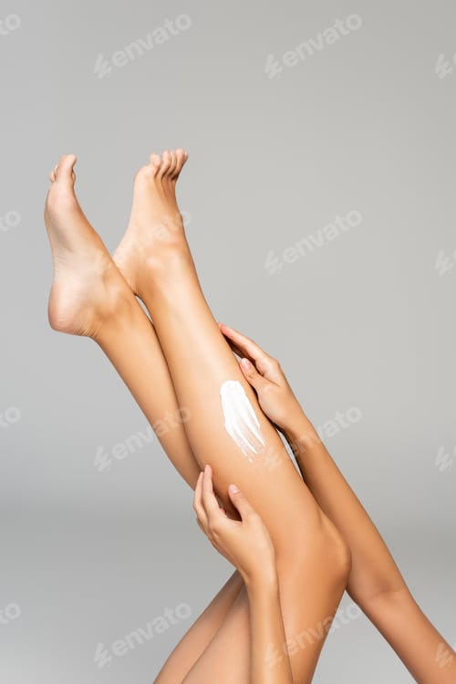 Preview: Cropped view of female legs in air with cream isolated on grey background