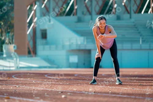 Preview: Asian athlete checking smartwatch after training on running track