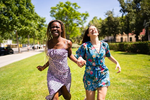 Preview: Two multiethnic women laughing while running holding hands outdoors