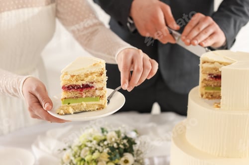 Preview: Newlyweds cutting wedding cake at table indoors, closeup