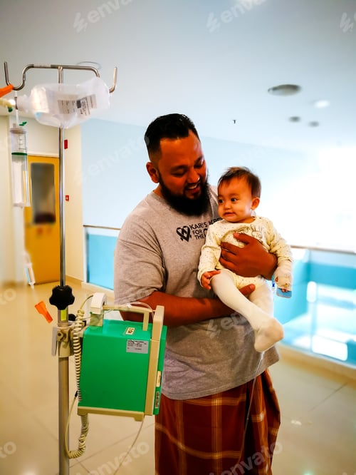 Preview: father holding sick child attached to the intravenous machine, walking in the hospital.