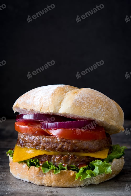 Preview: Delicious burger showing beef, cheddar, lettuce, tomato and red onion on rustic wooden table