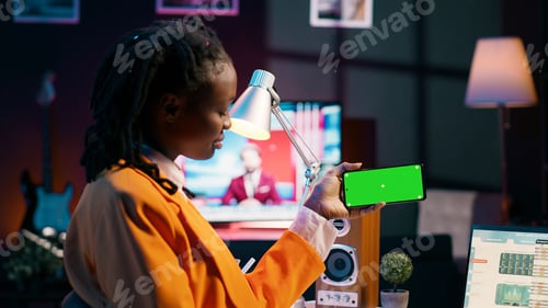 Preview: African american girl holds phone with isolated greenscreen at home,