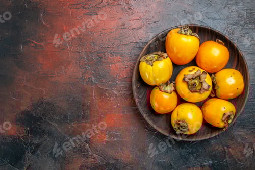 Preview: Above view of fresh organic natural yellow diospyros kaki on a brown plate on the left side of