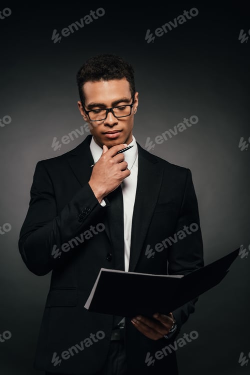 Preview: thoughtful african american businessman reading documents on dark background