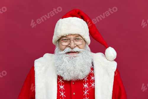 Preview: Happy old Santa Claus looking at camera standing on red background, headshot.