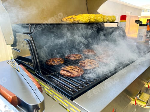 Preview: Hamburger Meat Patties being grilled on metal silver grill with smoke and corn for barbecue.