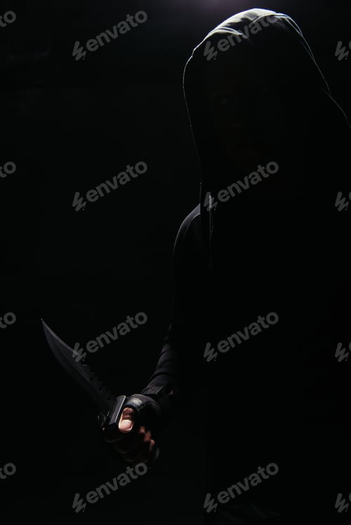 Preview: Silhouette of bandit in hood holding knife in lighting isolated on black