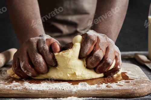 Preview: Unrecognizable male kneads dough on wooden counter, bakes delicious pastry, uses high quality flour.