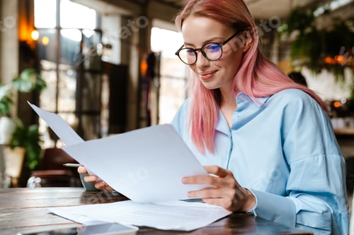 Preview: Young beautiful woman with pink hair doing paperwork in cafe