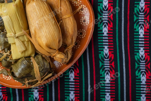 Preview: Different tamales in a clay dish on a tablecloth with the colors of the Mexican flag.