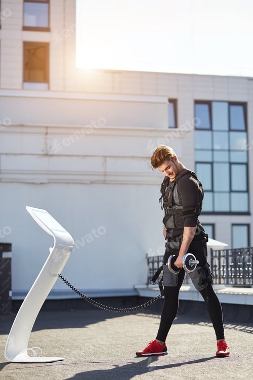 Preview: cheerful sportsman standing near the EMS machine and doing exercises