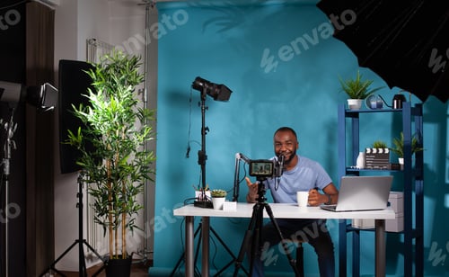 Preview: Wide view of vlogging studio setup with smiling vlogger interacting with audience sitting at desk