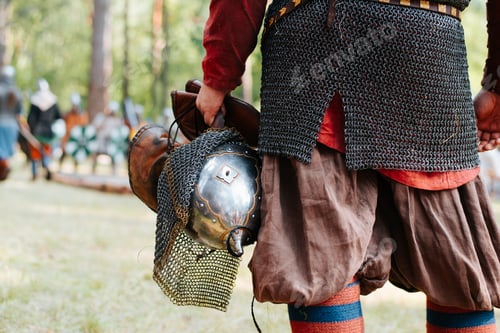 Preview: Close-up of a viking in chainmail holding a steel medieval helmet while standing