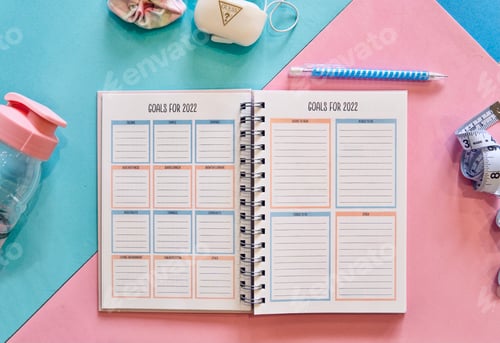 Preview: Overhead view of an open planner to goal pages for all areas of life on a pink and green background