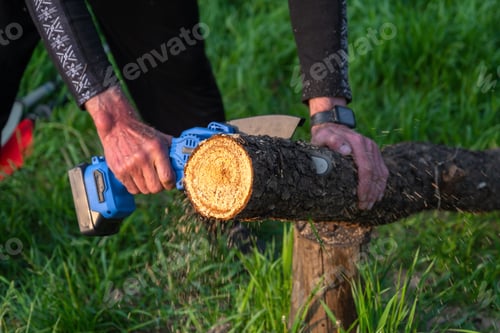 Preview: Hand-held portable camping electric saw on a battery for cutting firewood and wood. Close-up, a hand