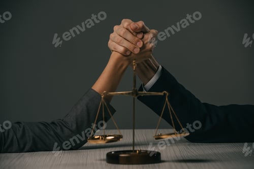 Preview: partial view of businessman and businesswoman arm wretsling on wooden table with scales of justice