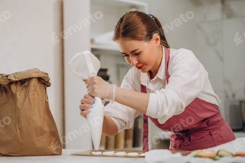 Preview: cooking, food and baking concept - chef with confectionery bag squeezing cream filling to macarons
