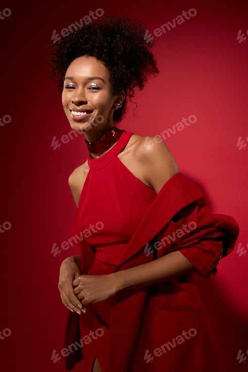 Preview: Joyful young woman in red attire smiling against a vibrant red backdrop
