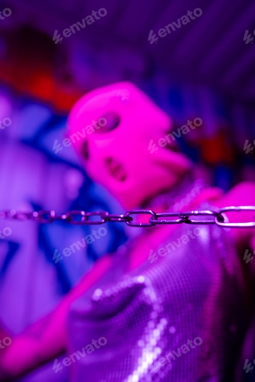 Preview: selective focus of silver chain near blurred woman in balaclava in blue and purple lighting