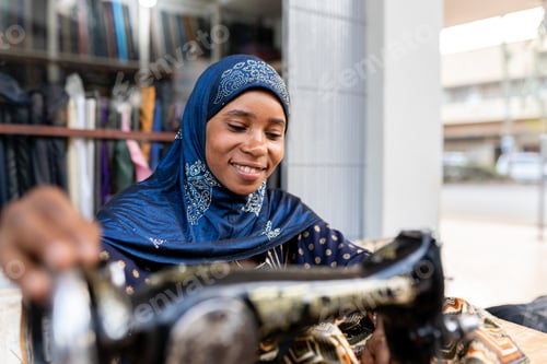 Preview: African dressmaker woman working with sewing machine at outdoor atelier