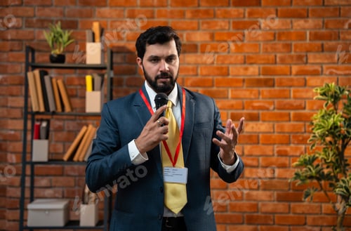 Preview: Bearded Indian CEO giving formal speech using mic while standing in cozy office environment